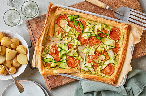 Bake a simple dinner with this quick tomato and courgette tart recipe. Pesto and créme fraîche make a herby, creamy base on top of buttery puff pastry for the colourful veggie topping.